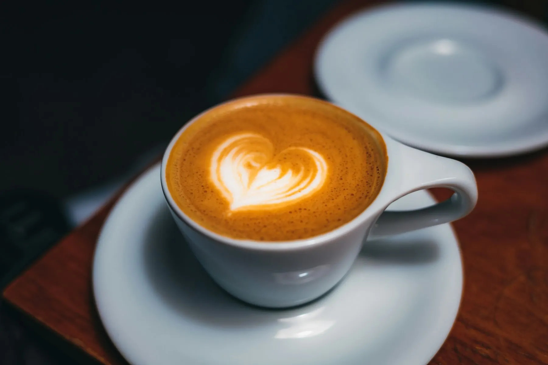 A cup of coffee with a heart poured in the foam, on a wooden table